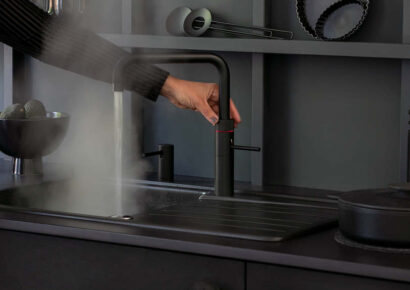 Schwarze Küche mit schwarzem Kochendwasserhahn von Quooker. Eine Hand bedient ihn.
