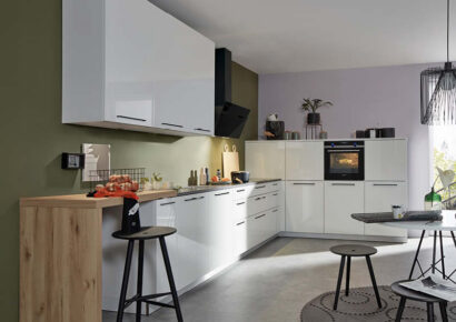 Klassische L-Küche mit Steinarbeitsplatte in hochglanz-weiß mit grüner Rückwand.